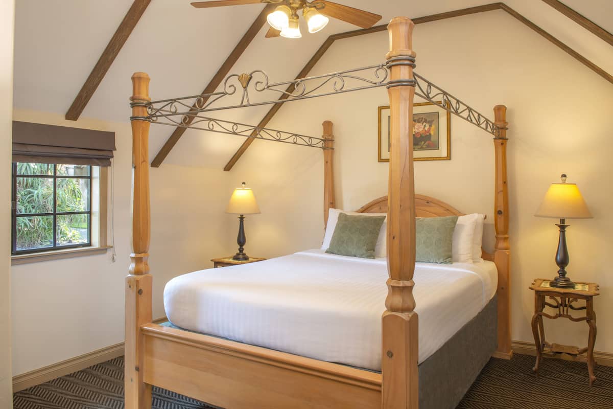 A four-poster bed with a wooden frame, two bedside tables with lamps, and a ceiling fan.