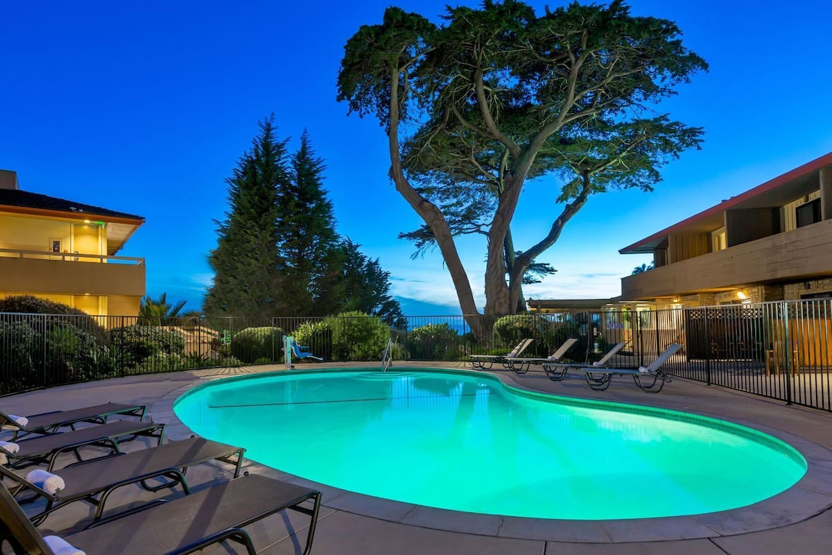 A swimming pool with lounge chairs, a large tree, and buildings in the background.