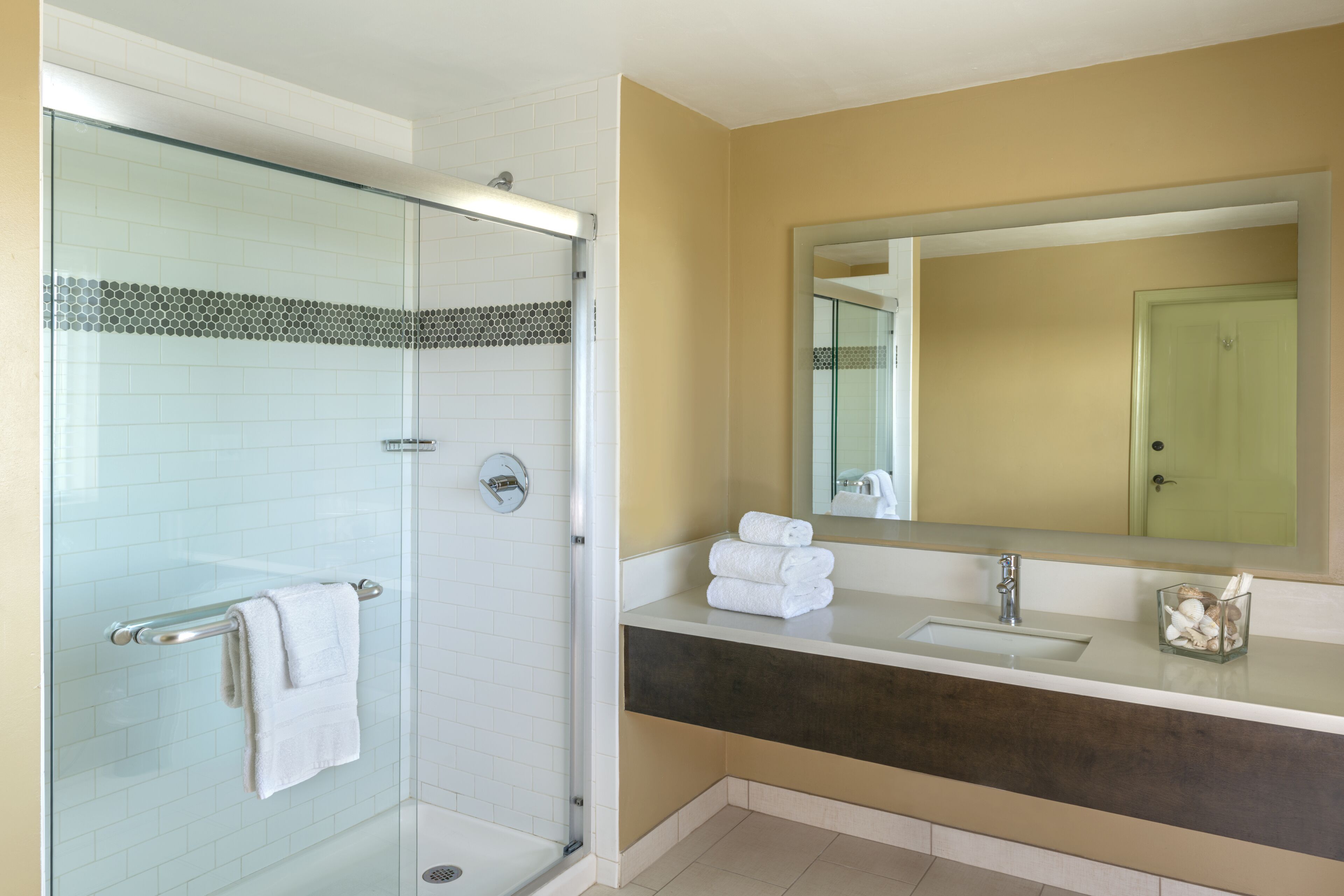 A modern bathroom with a glass shower enclosure, a vanity with a dark countertop, and a large mirror above the sink.