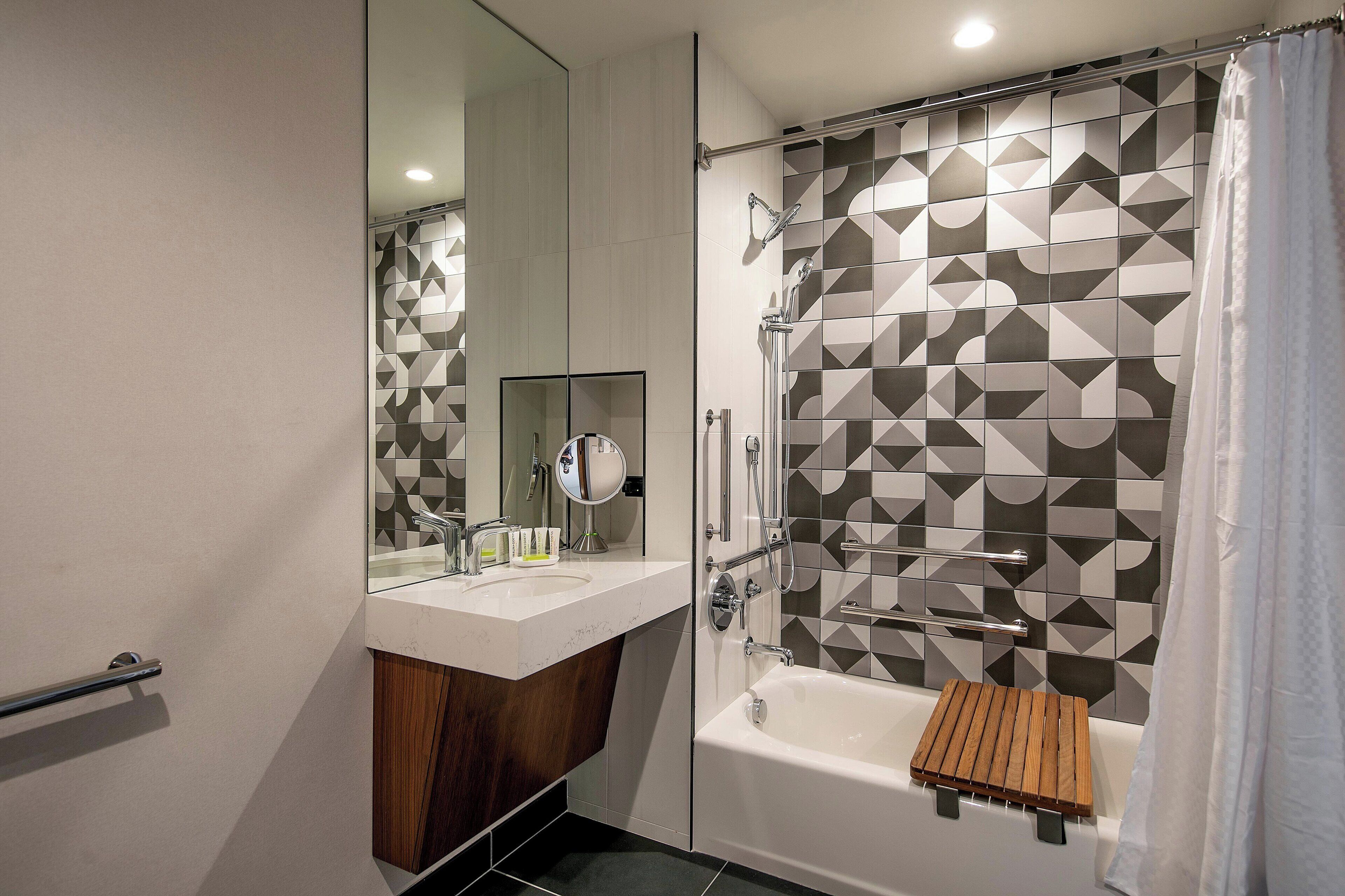 A modern bathroom with a shower, a bathtub, a vanity with a mirror, and a geometric-patterned wall.