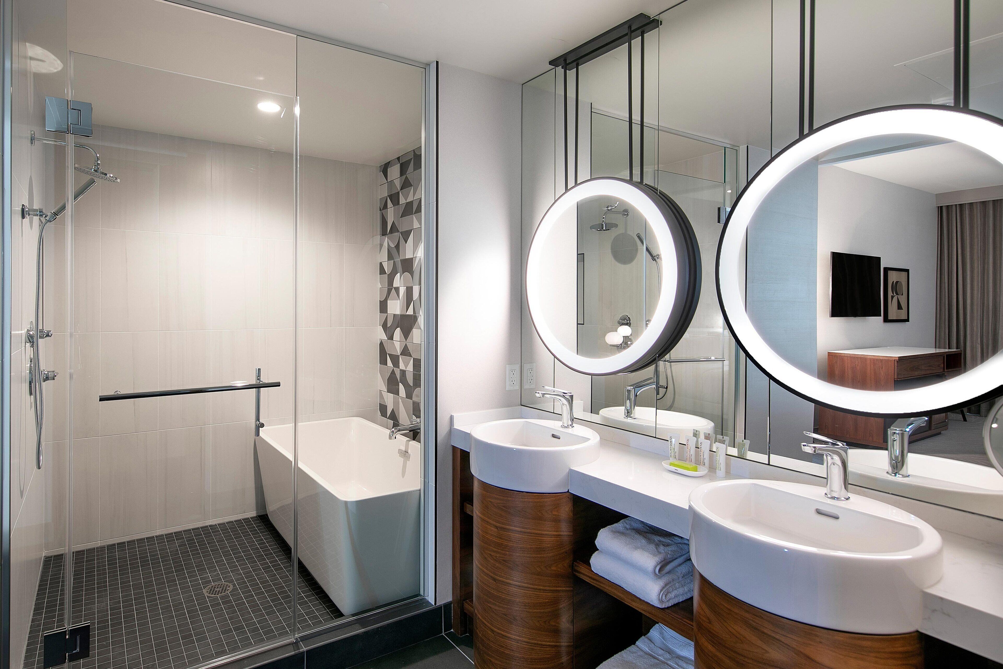 A modern bathroom with a glass-enclosed shower, a bathtub, and two sinks with mirrors.