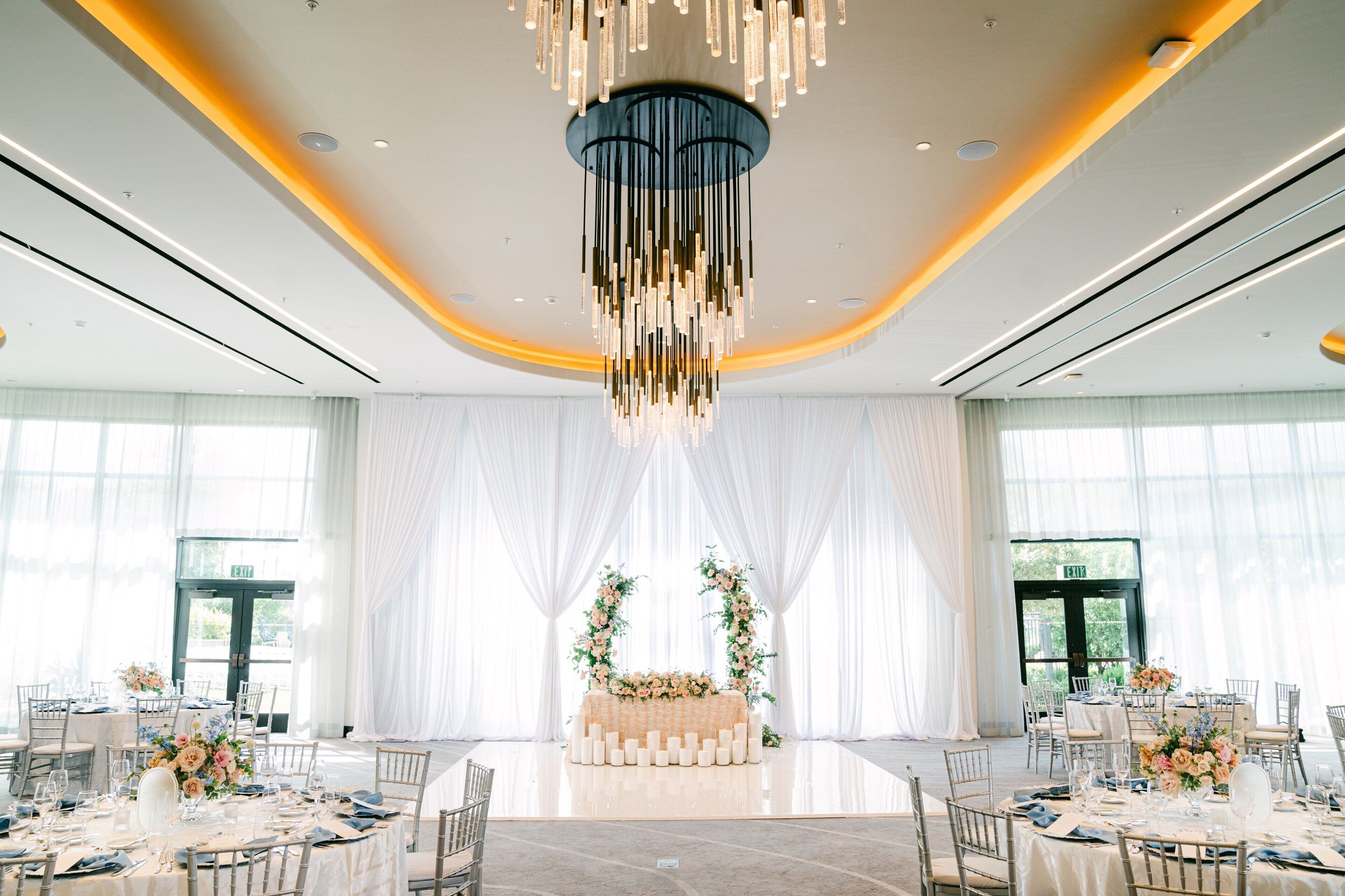Un salón de banquetes con mesas redondas, un arreglo floral central y una moderna lámpara de araña.
