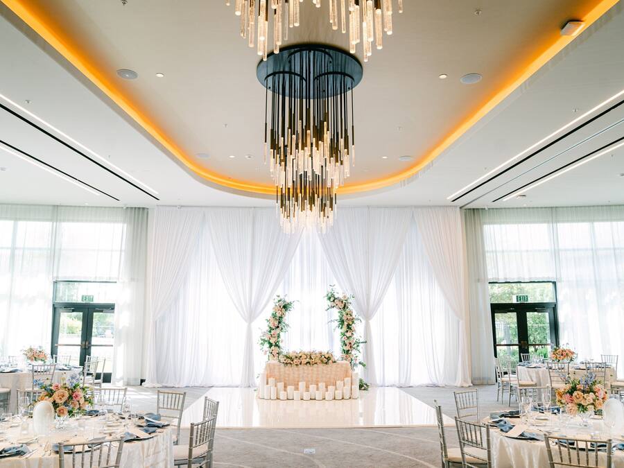 Un salón de banquetes con mesas redondas, un arreglo floral central y una moderna lámpara de araña.