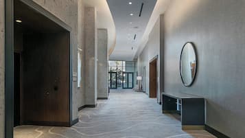 A modern hotel corridor with a patterned carpet, a wooden door, a bench, and a mirror on the wall.