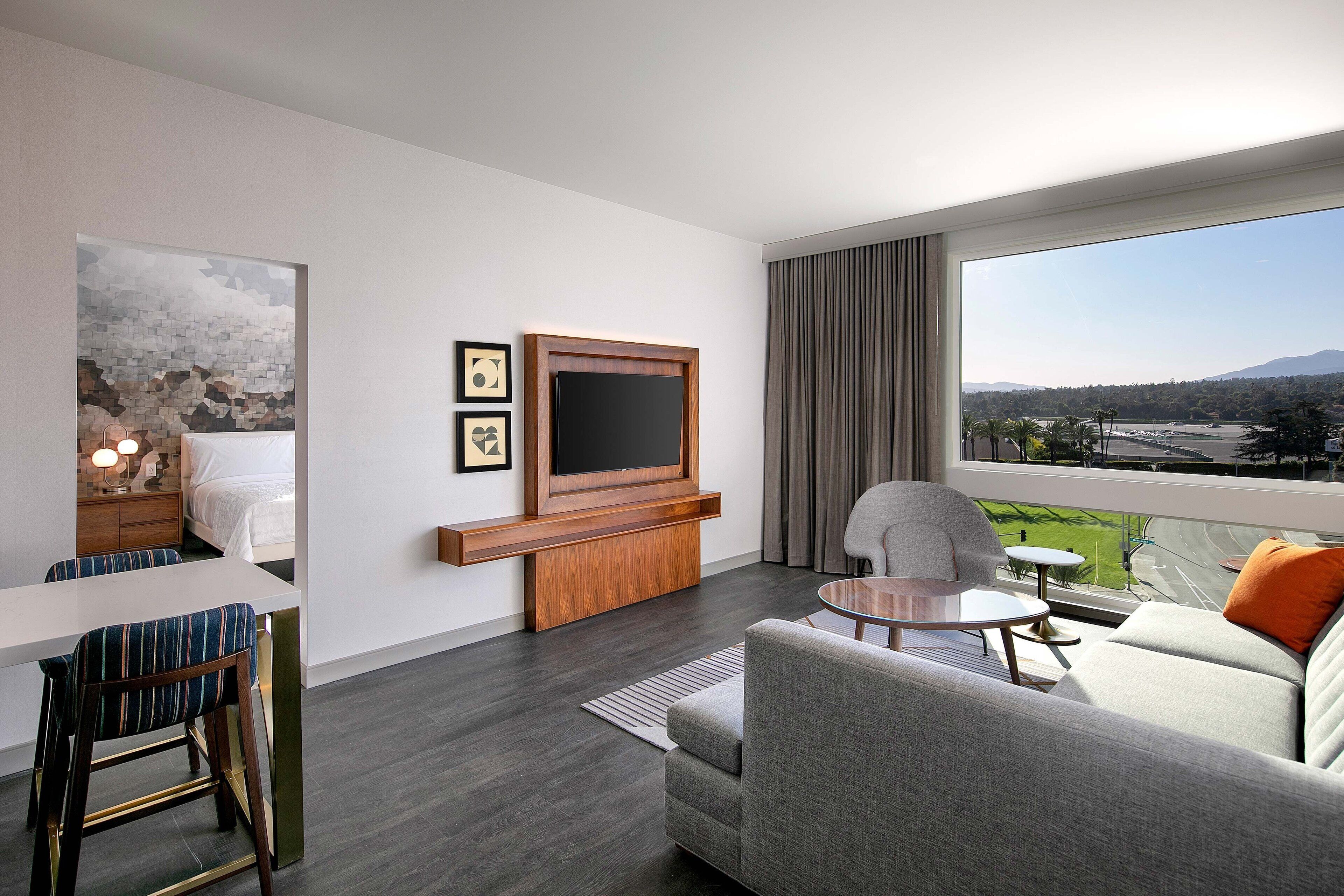 A modern living room with a flat-screen TV, a sofa, a dining table, and a view of a cityscape.