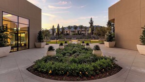 A modern building with large windows and a landscaped courtyard with various plants and seating areas. - Le Méridien Pasadena Arcadia (Arcadia)
