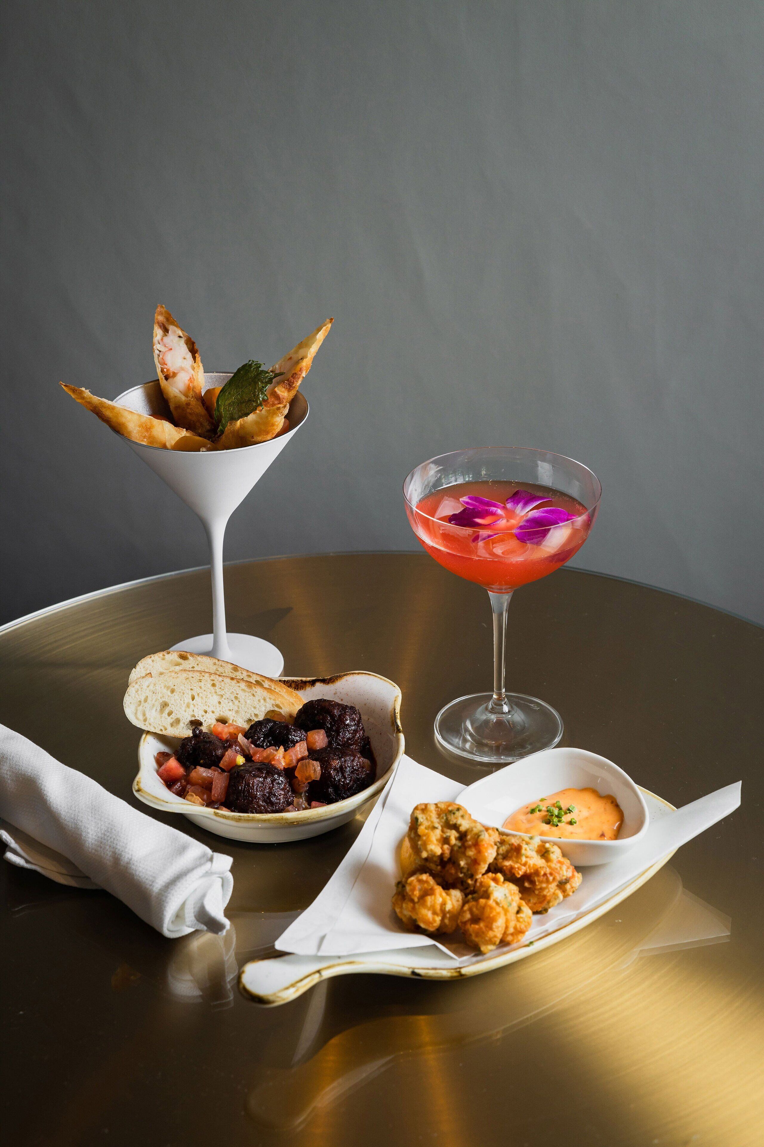 A table with a martini glass, a bowl of breaded chicken, and a bowl of mixed vegetables.