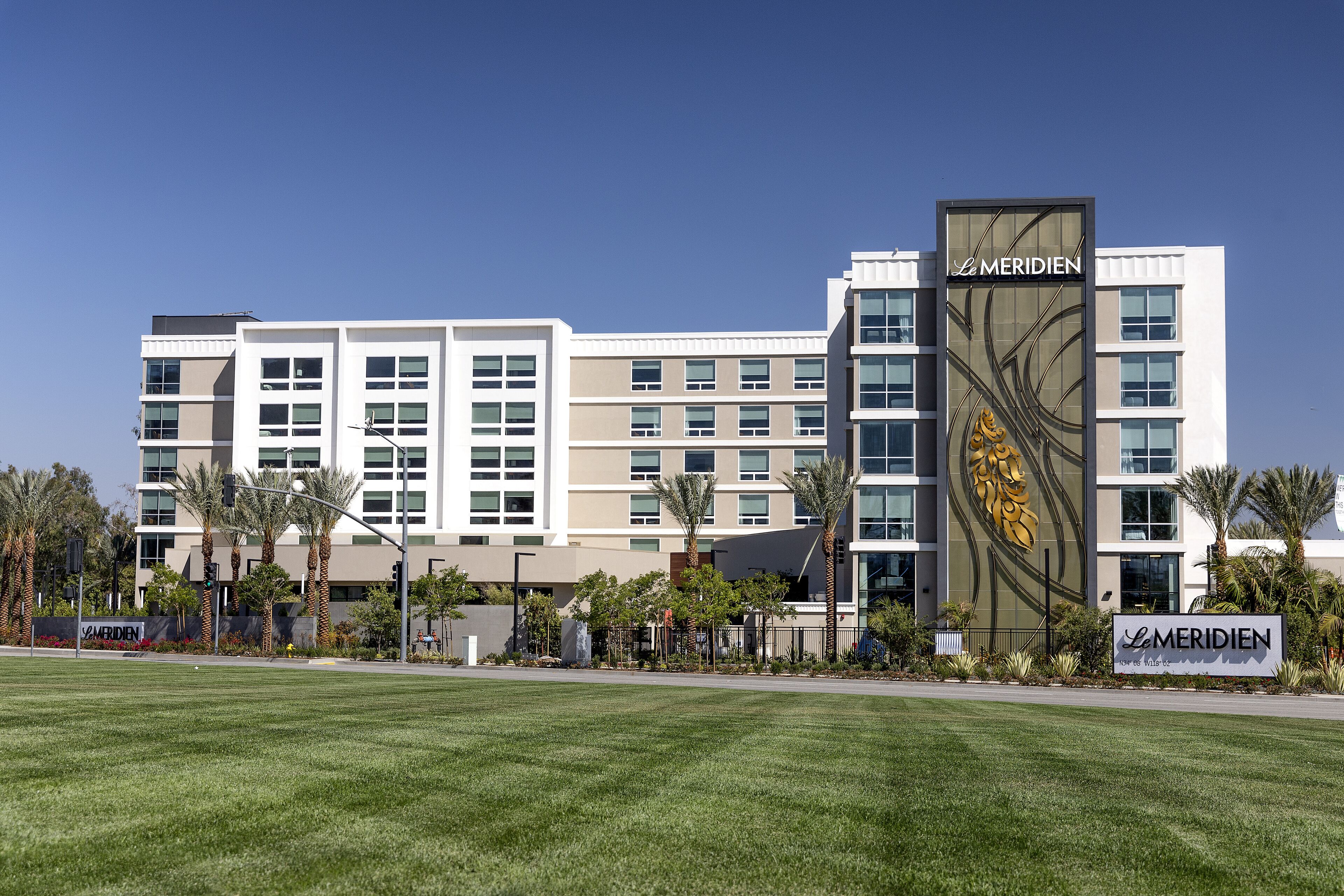 A modern hotel with multiple floors, a prominent logo, and a well-maintained lawn in front.