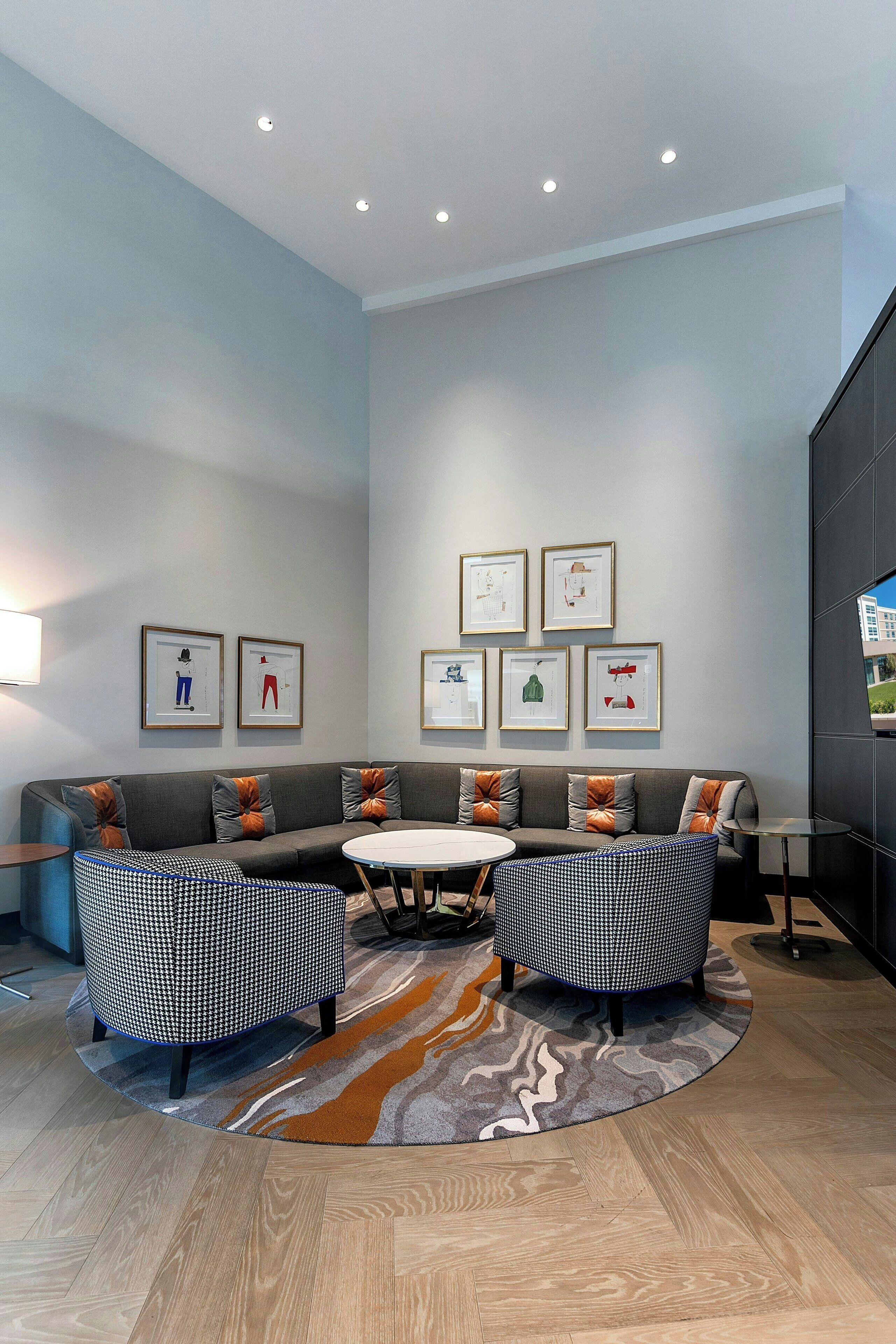 Un espace de détente moderne avec un canapé gris, deux fauteuils, une table ronde et des œuvres d’art encadrées accrochées au mur.