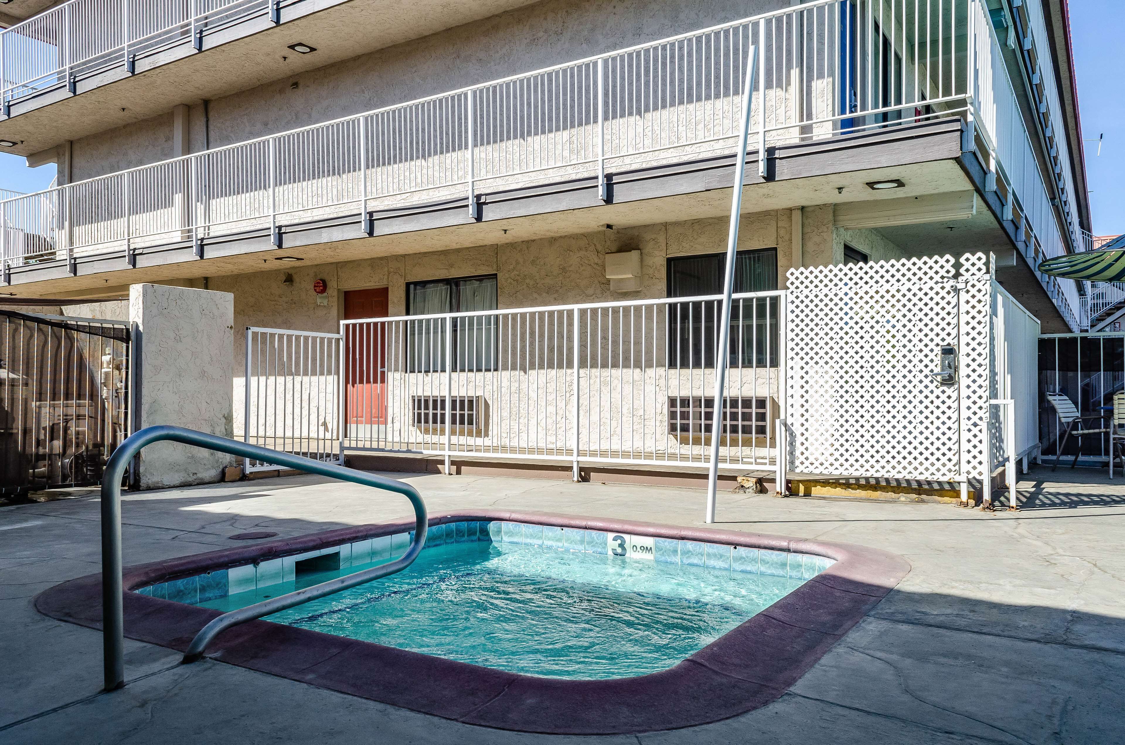 A swimming pool with a metal ladder, a white fence, and a building with balconies in the background.