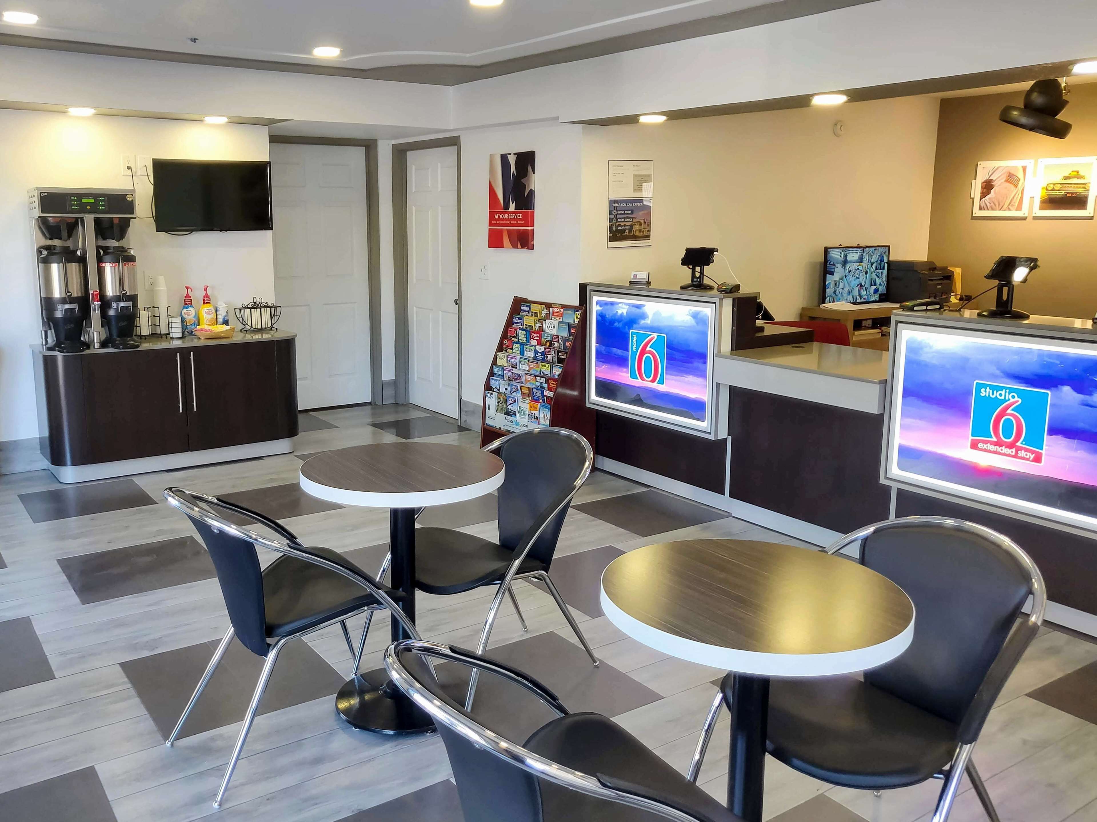 A modern hotel lobby with a reception desk, coffee machines, and seating area.