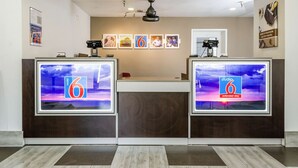 A hotel reception area with two large digital displays, a ceiling fan, and framed pictures on the wall. - Motel 6 Fresno, CA - Yosemite Hwy (Fresno)