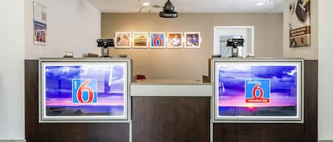 Un espace d’accueil d’hôtel doté de deux grands écrans numériques, d’un ventilateur de plafond et de tableaux encadrés accrochés au mur.