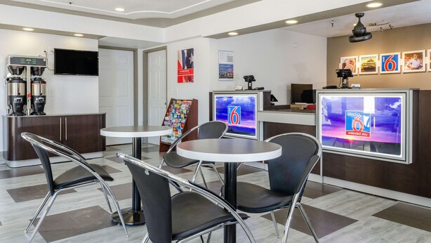 A modern hotel lobby with a coffee machine, a TV displaying a news channel, and a reception desk. - Motel 6 Fresno, CA - Yosemite Hwy (Fresno)