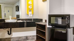 A modern bathroom with a black countertop sink, a mirror, a yellow towel warmer, and a microwave on a refrigerator. - Motel 6 Fresno, CA - Yosemite Hwy (Fresno)