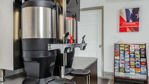 A coffee machine with a drip tray, a wall-mounted sign with 'ECAF' and 'AT YOUR SERVICE', and a stand with travel brochures. - Motel 6 Fresno, CA - Yosemite Hwy (Fresno)
