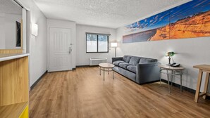 Een moderne woonkamer met een bank, een klein rond tafeltje, een lamp en een schilderij aan de muur.