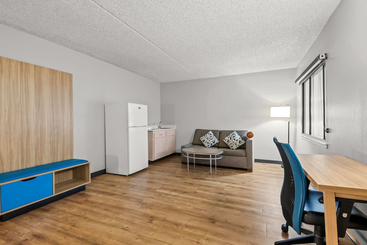 A modern apartment with a kitchenette, a dining area with a table and chairs, a sofa with patterned cushions, and a blue bench.