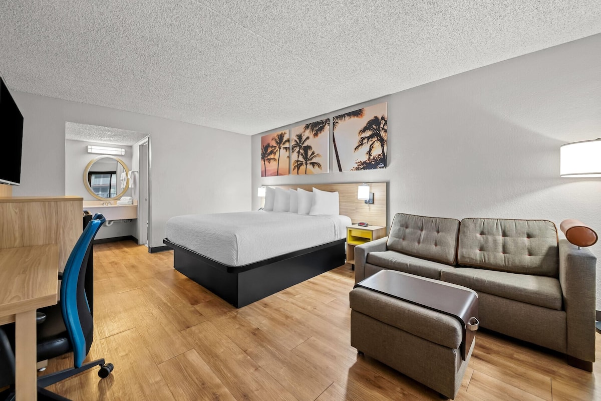A modern hotel room with a bed, a sofa, a desk, and a chair.