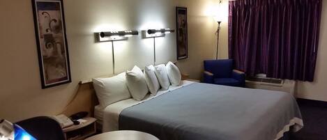A hotel room with a large bed, bedside lamps, a desk with a chair, a round table, and a large window with curtains.