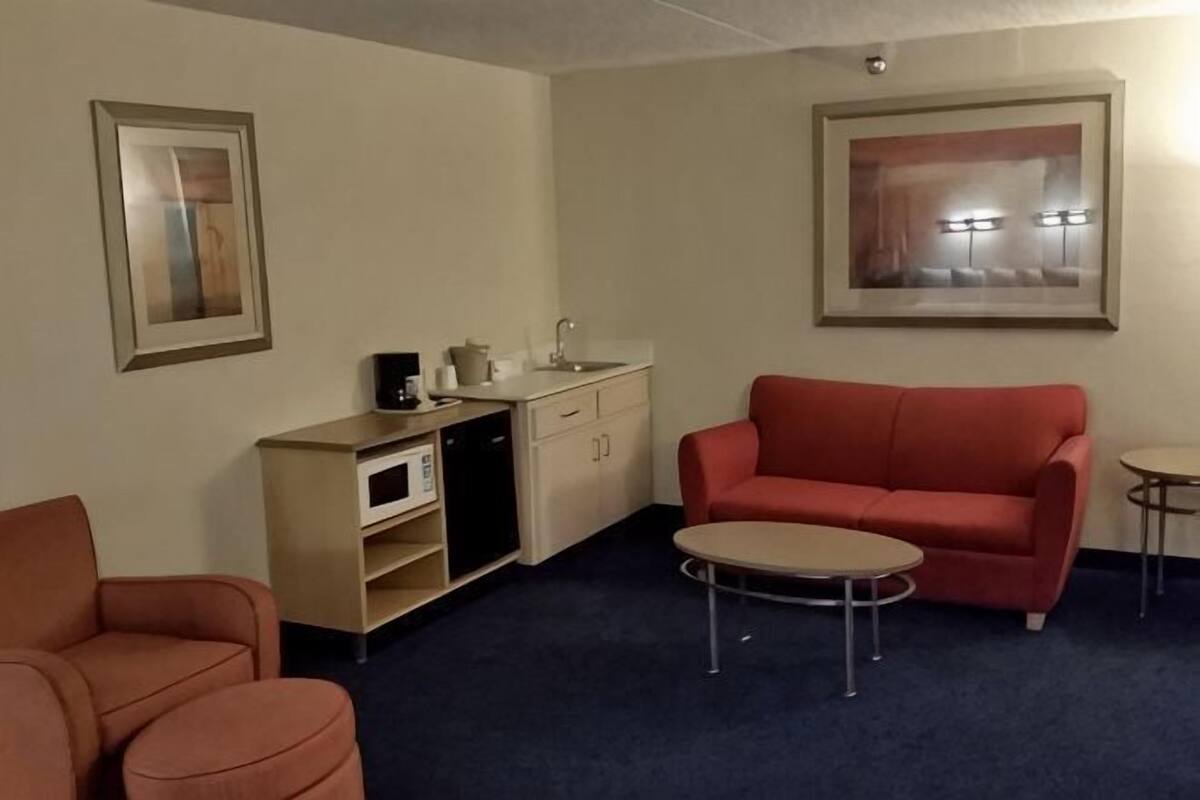 A compact living space with a kitchenette, a red sofa, a small round table, and a single chair.