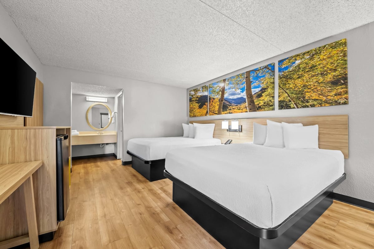 A hotel room with a large bed, two bedside tables, a TV, a mirror, and a wall with three paintings.