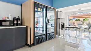 Een moderne keuken met een magnetron, koffieapparaat en twee koelkasten, waarvan er twee zijn gelabeld 'SNACKS' en 'KOUD'.