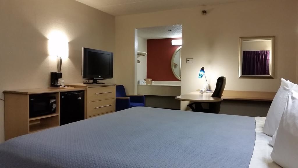 A hotel room with a large bed, a desk with a chair, a television, a desk lamp, a mirror, and a window with curtains.