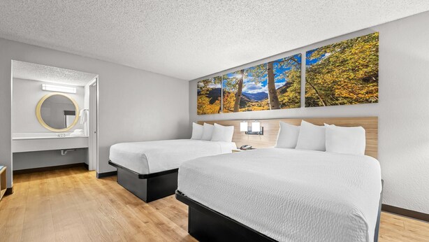 Een hotelkamer met twee bedden, een grote spiegel, een kunstwerk aan de muur en een houten vloer.