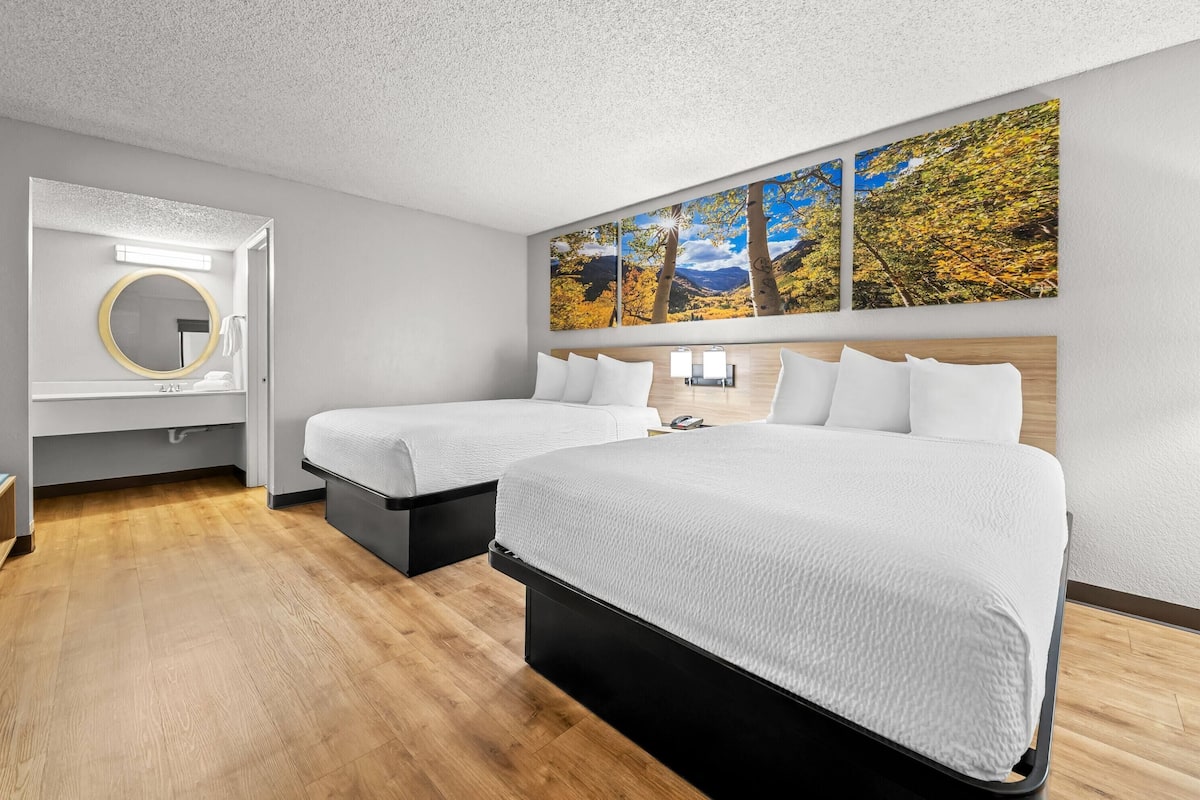 A hotel room with two beds, a large mirror, a wall-mounted artwork, and a wooden floor.