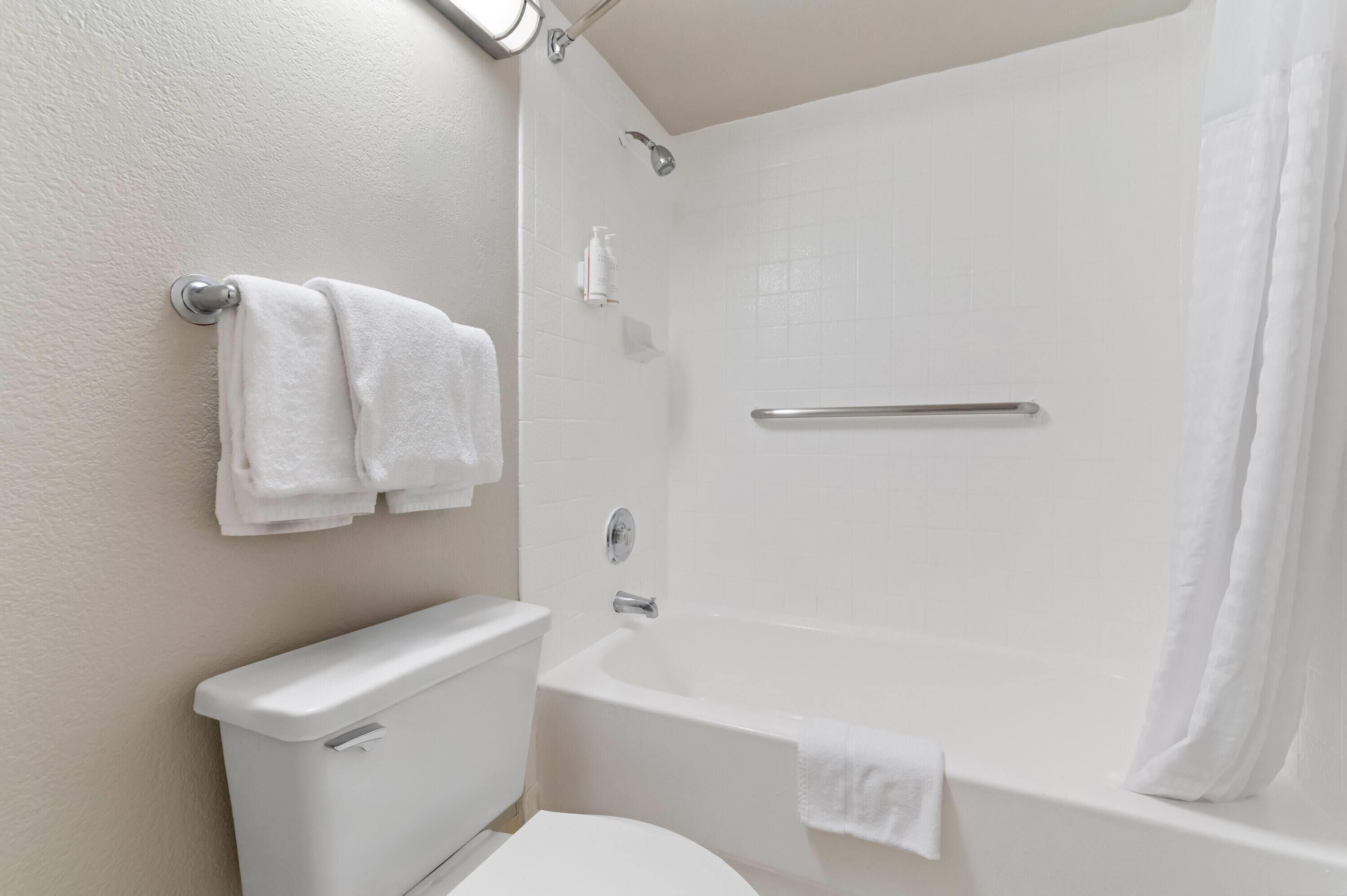 Un baño con inodoro, bañera con cortina de ducha y dos toallas colgadas en la pared.
