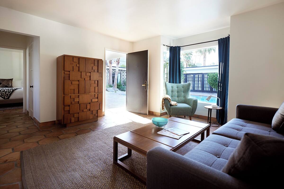 A living room with a sofa, a coffee table, and a chair. There is a view of a pool outside.