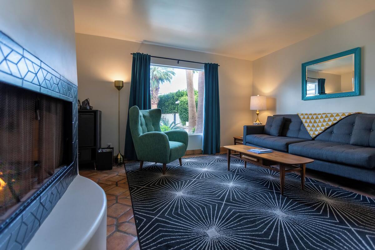 A modern living room with a fireplace, a green armchair, a sofa, and a patterned rug.