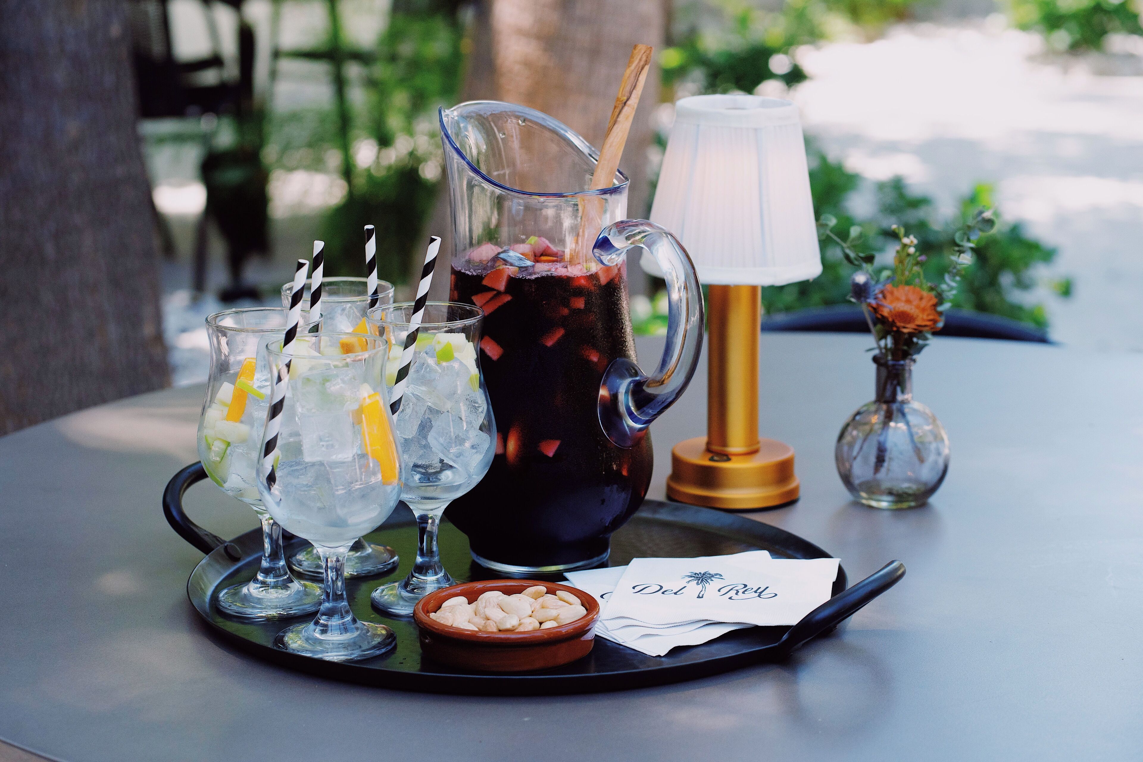 Een dienblad met een pitcher ijskoude drankjes, glazen, een kleine schaal met noten en een kandelaar.