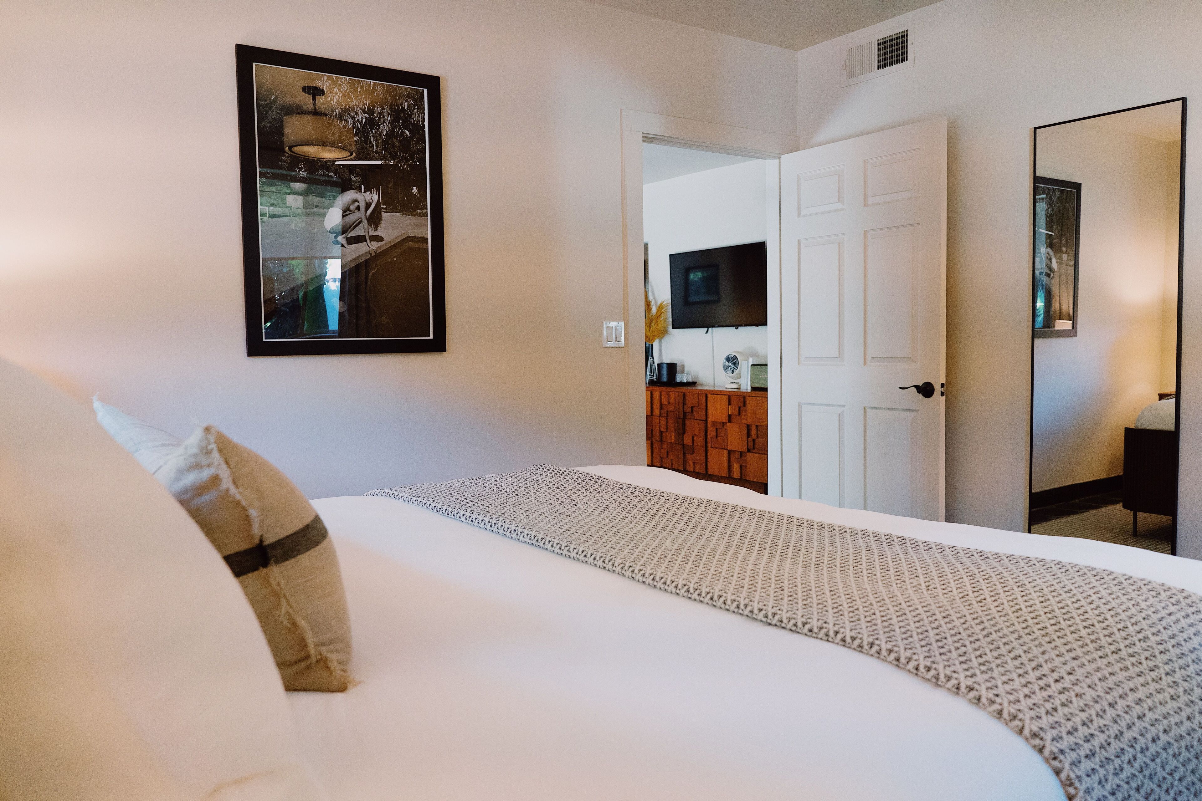 A hotel room with a bed, a framed picture on the wall, a television, and a door leading to another room.