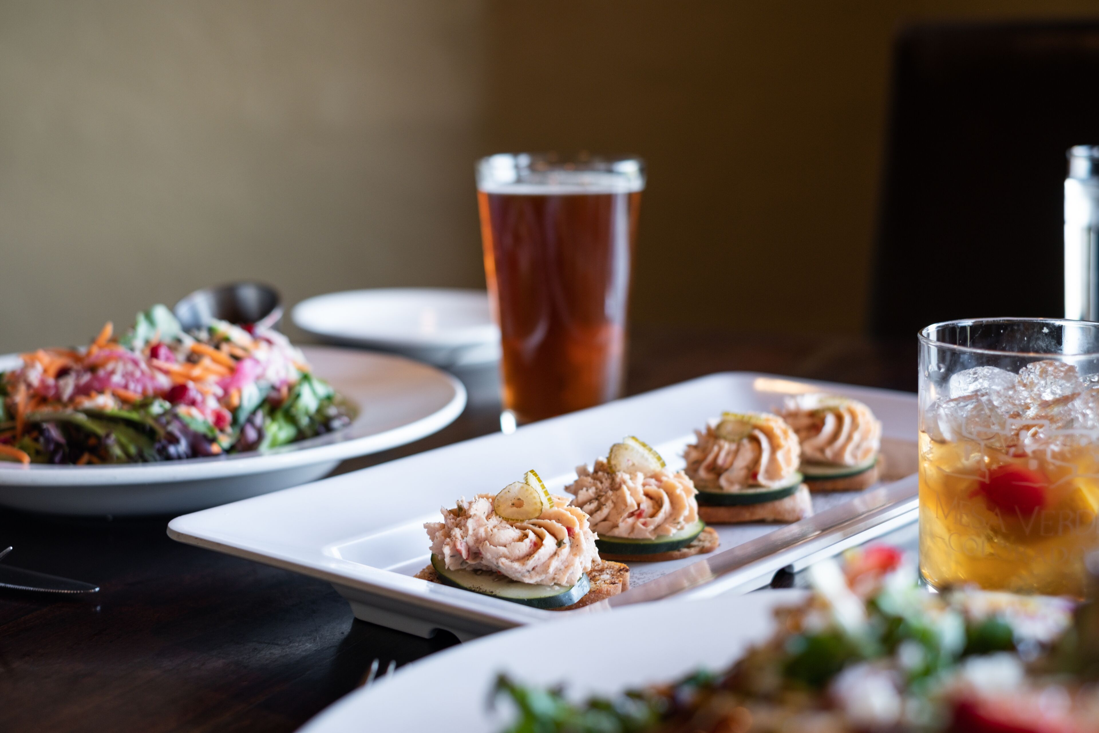 A dining table with a variety of dishes, including a salad, a plate of appetizers, and a glass of iced tea.