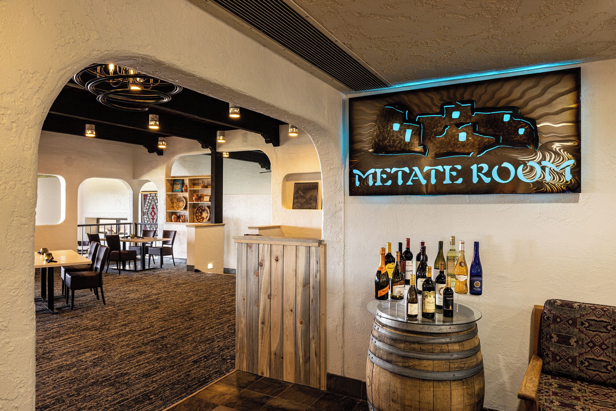 A restaurant interior with a bar area, wooden furniture, and a neon sign reading "METATE ROOM".