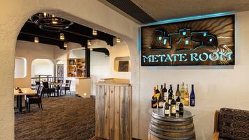 A restaurant interior with a bar area, wooden furniture, and a neon sign reading "METATE ROOM".