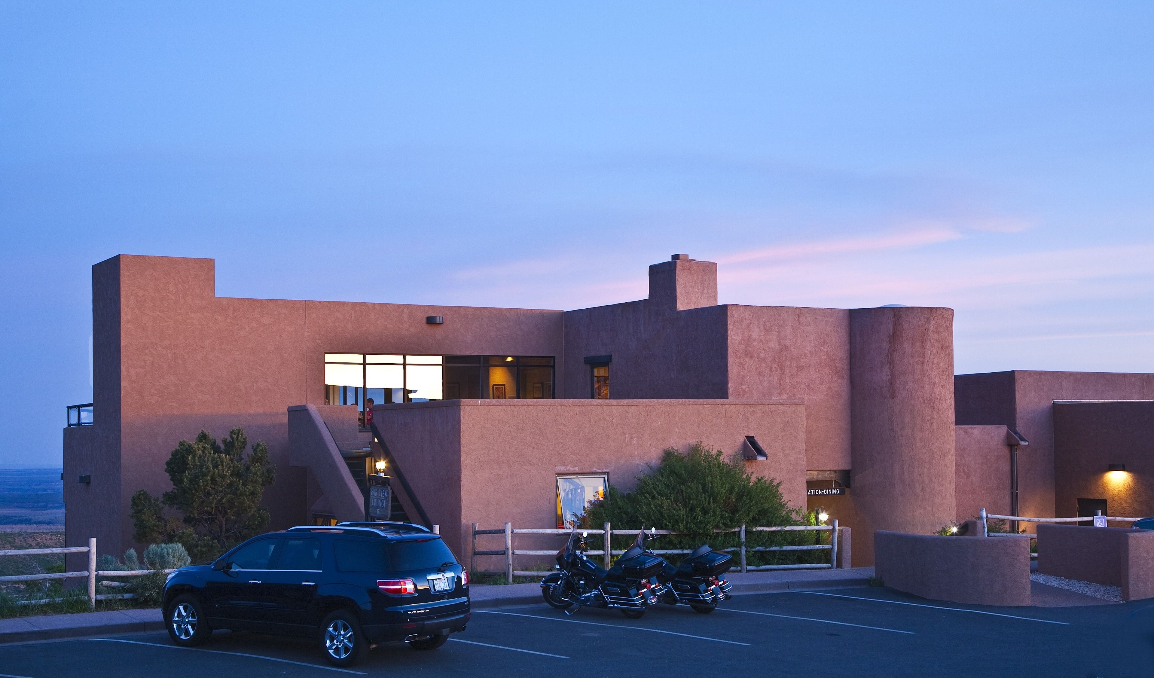 Il s’agit d’un bâtiment moderne doté d’un toit plat et d’une grande fenêtre. Un SUV noir est garé devant, et une moto est stationnée sur le côté.