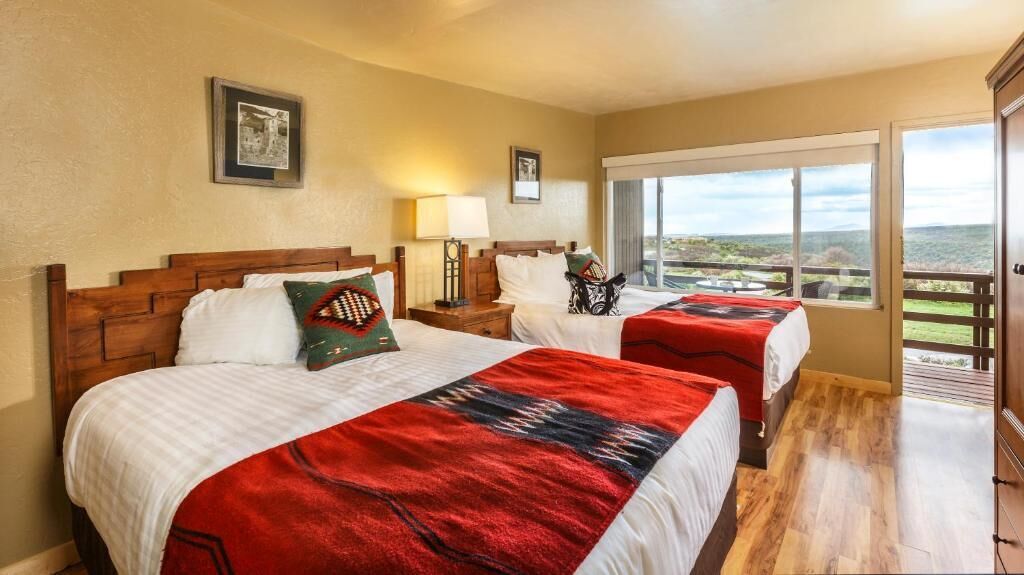 A hotel room with two beds, a balcony with a view, and a wooden floor.