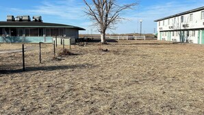 Un edificio de techo plano, con una zona cercada y un campo árido.