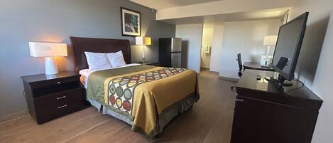 A hotel room with a bed, bedside tables, a desk, a chair, a television, and a refrigerator.