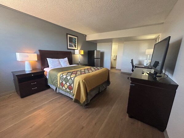 A hotel room with a bed, bedside tables, a desk, a chair, a television, and a refrigerator.