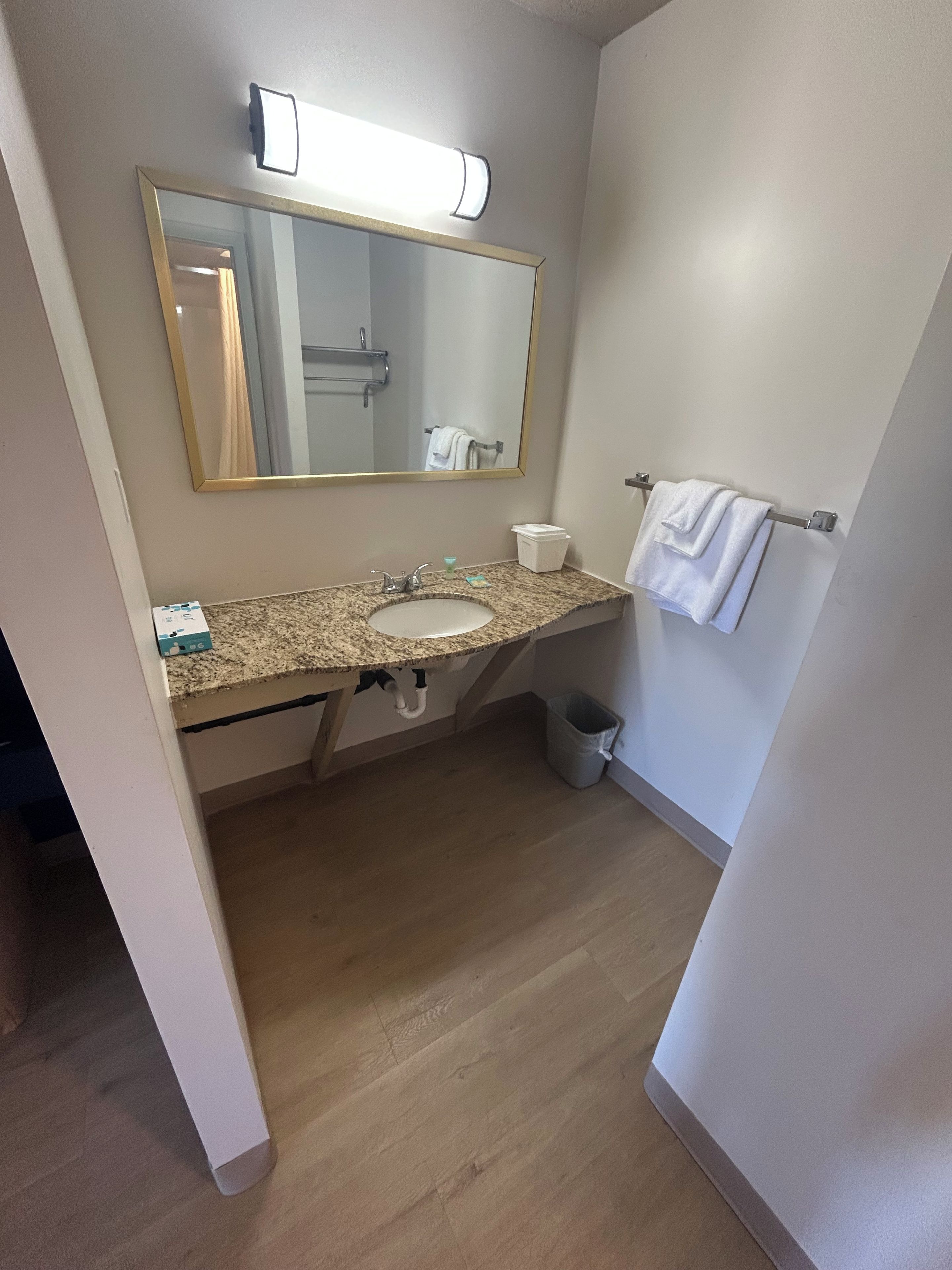 Een badkamer met een wastafel, spiegel, handdoekhouder en prullenbak.