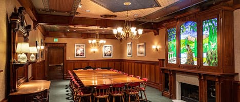 A conference room with a large wooden table, red chairs, chandeliers, framed pictures on the walls, and stained glass windows.