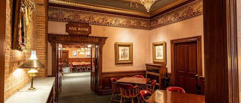 Habitación de hotel con candelabro, cartel que dice 'OAK ROOM' y zona de comedor con mesas y sillas.