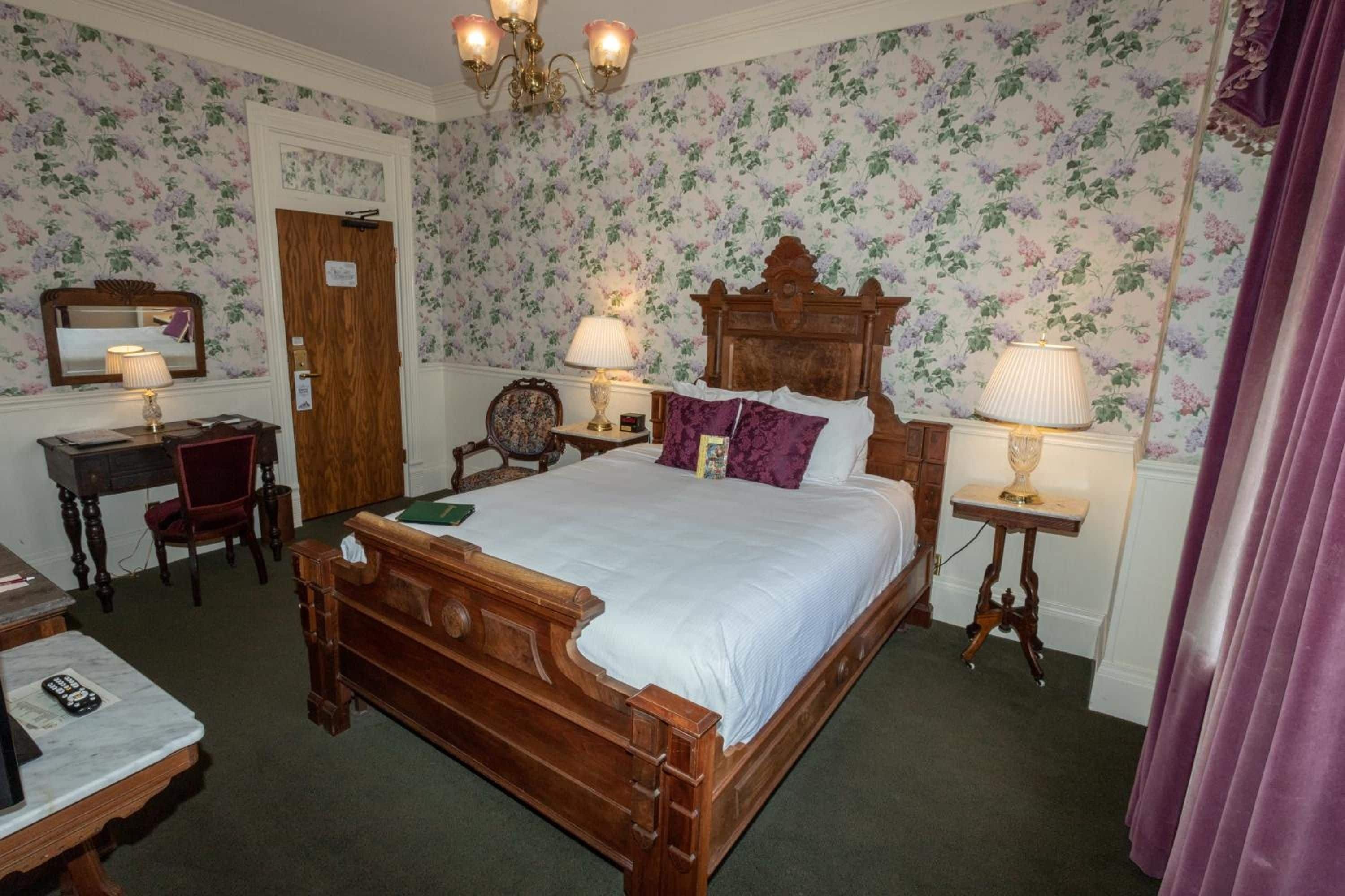 Una camera da letto tradizionale con un letto a baldacchino in legno, una scrivania con una sedia, uno specchio e un lampadario.