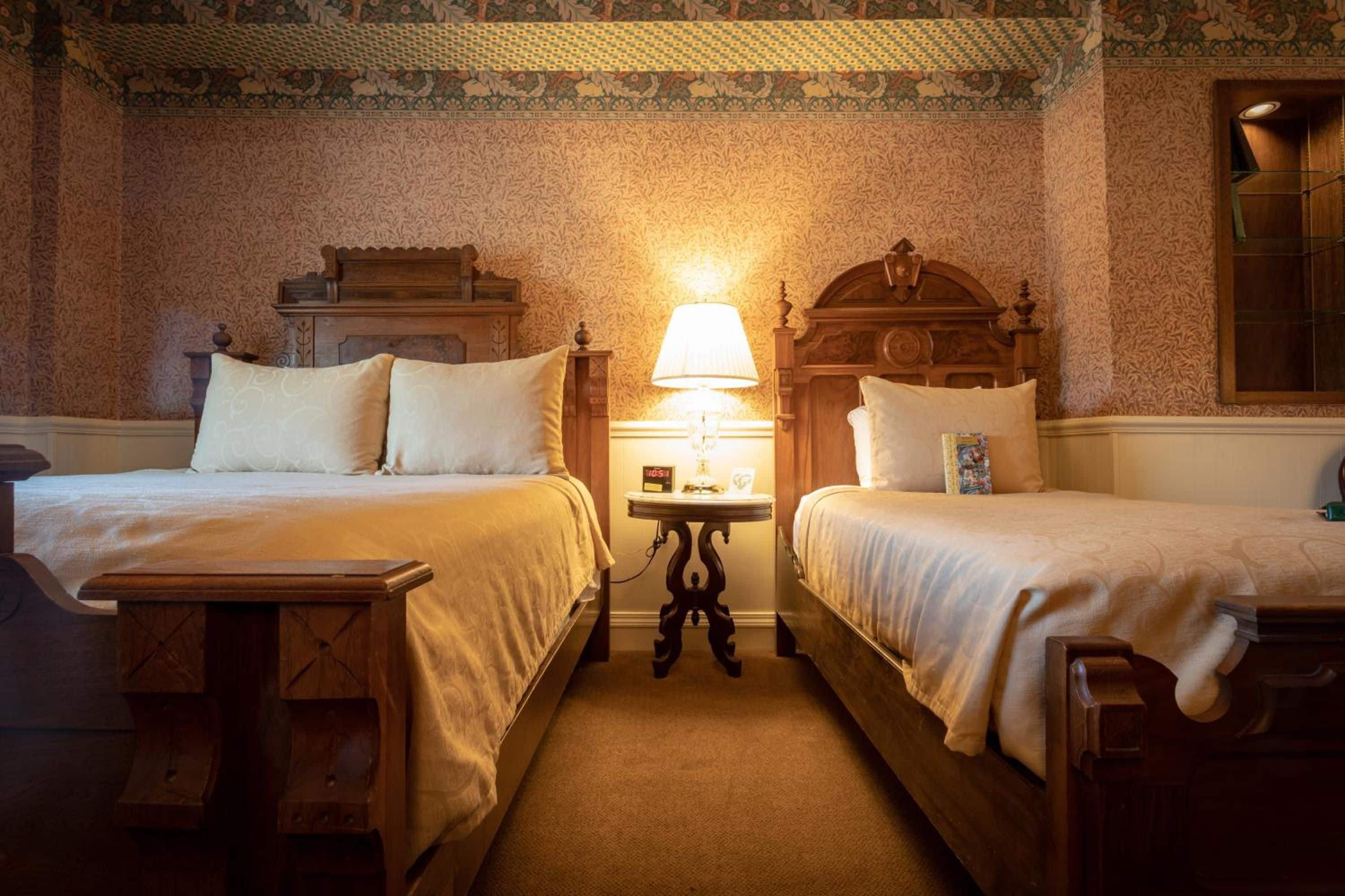 Ein Hotelzimmer mit zwei Betten, einem Nachttisch mit Lampe und einem hölzernen Kopfteil.