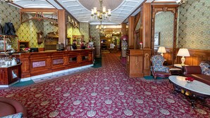 Un hall d’entrée spacieux, doté d’un tapis rouge à motifs, de meubles en bois et d’un lustre.