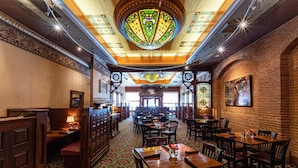 Un restaurant doté d’un tapis à motifs, de tables et de chaises en bois, et d’une grande fenêtre à vitraux.